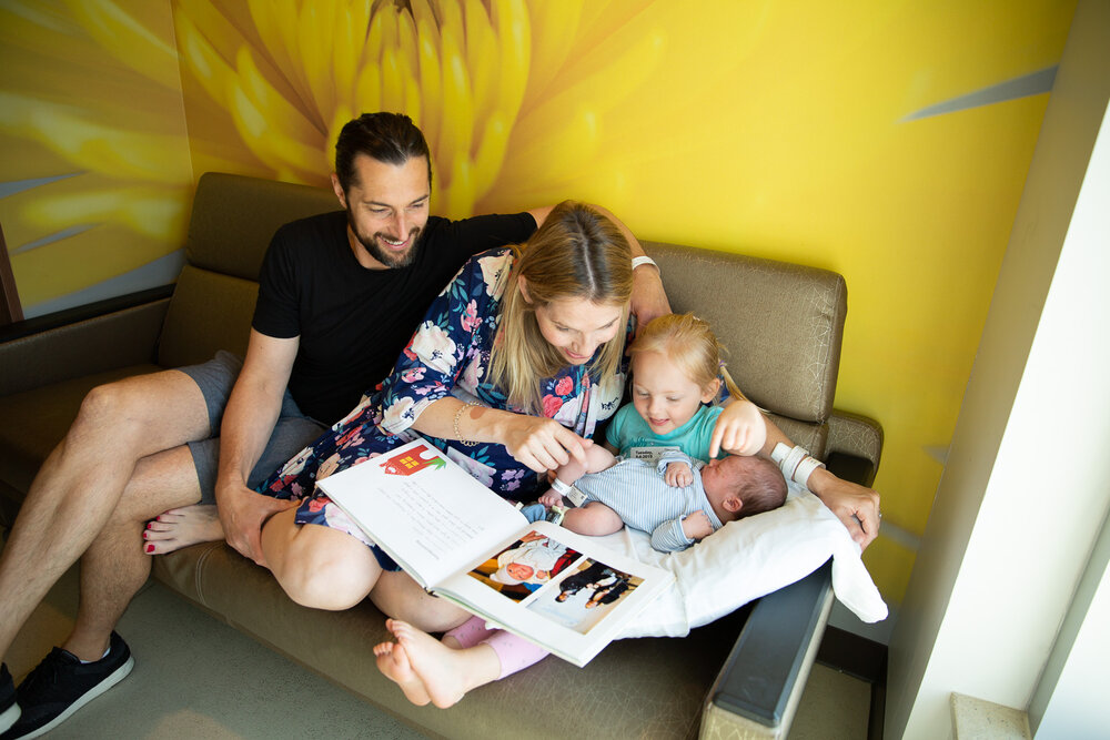 newborn baby in blue swaddle being help by younger sister looking at photo album with mom and dad at Minneapolis birth center