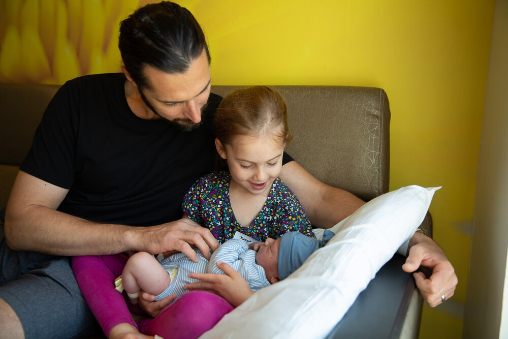 Father and daughter greeting the newest member of the family, a newborn boy held in his sistern's lap