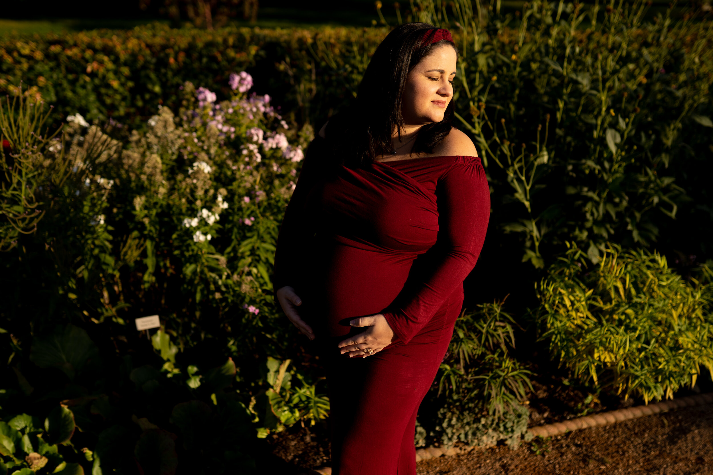 Mother to be wearing a stunning red dress posed at a Minneapolis botanical garden