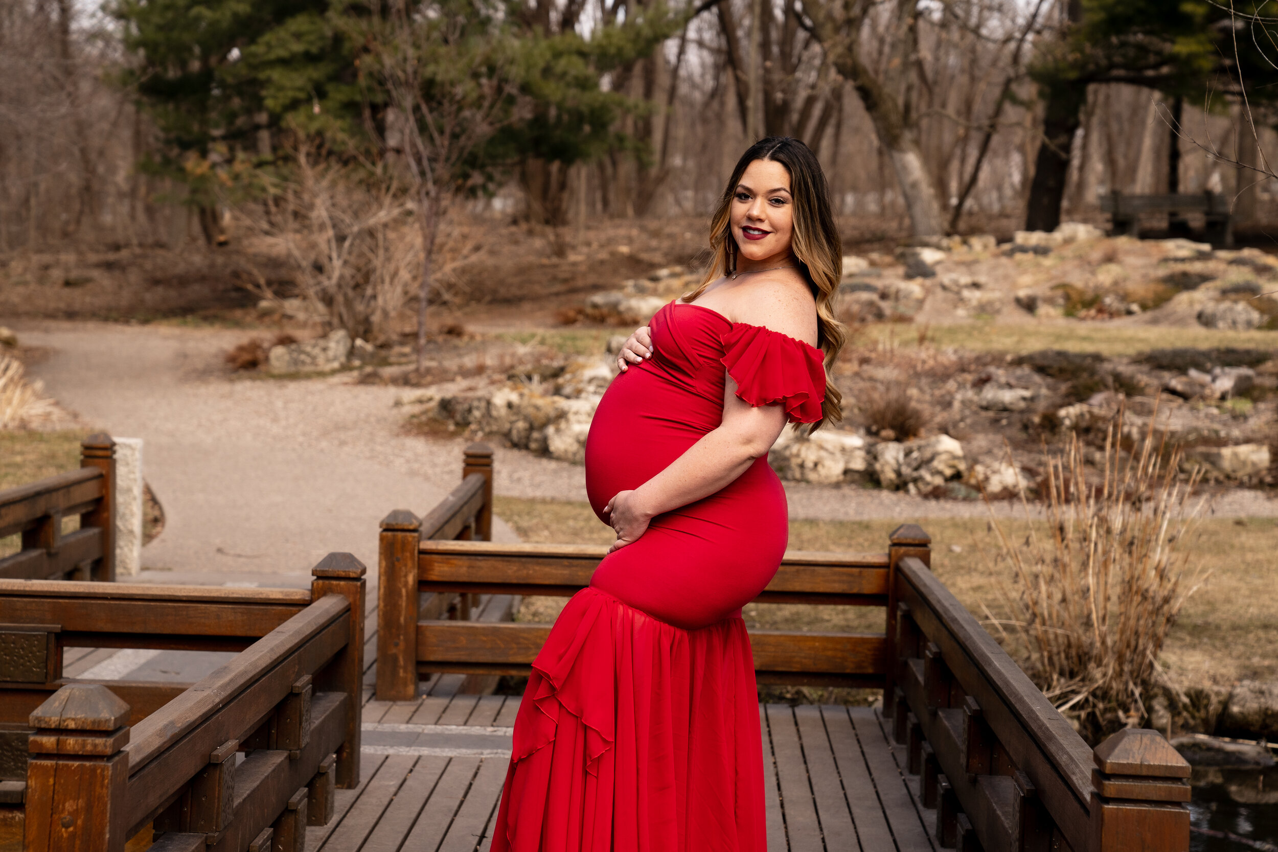 Mother to be in a vibrant red dress posed on a wooden walkway in Minneapolis