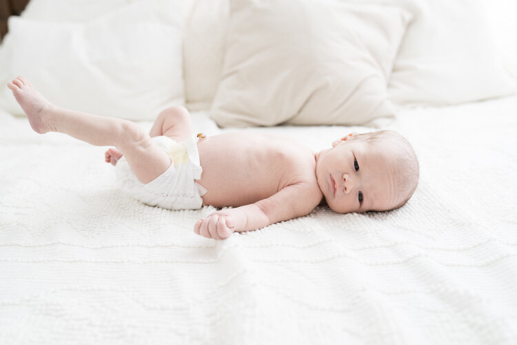 newborn baby boy on white bedspread wearing a white diaper looking directly at camera