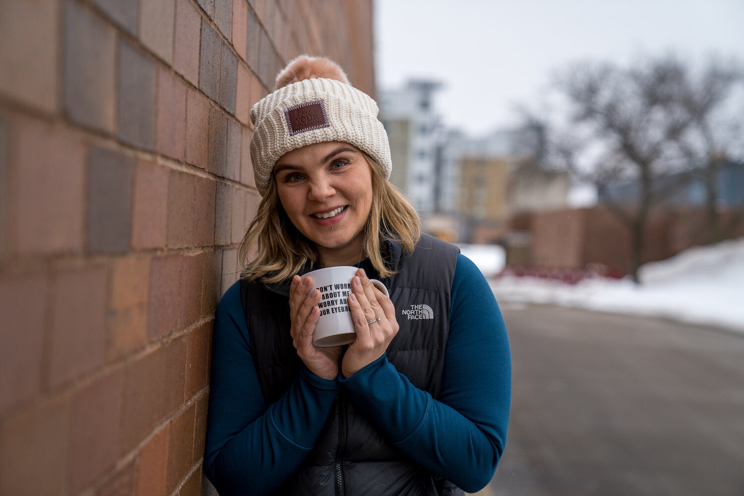 Woman in winter clothing smiling at the camera and leaning against a brick wall in Minneapolis Minnesota