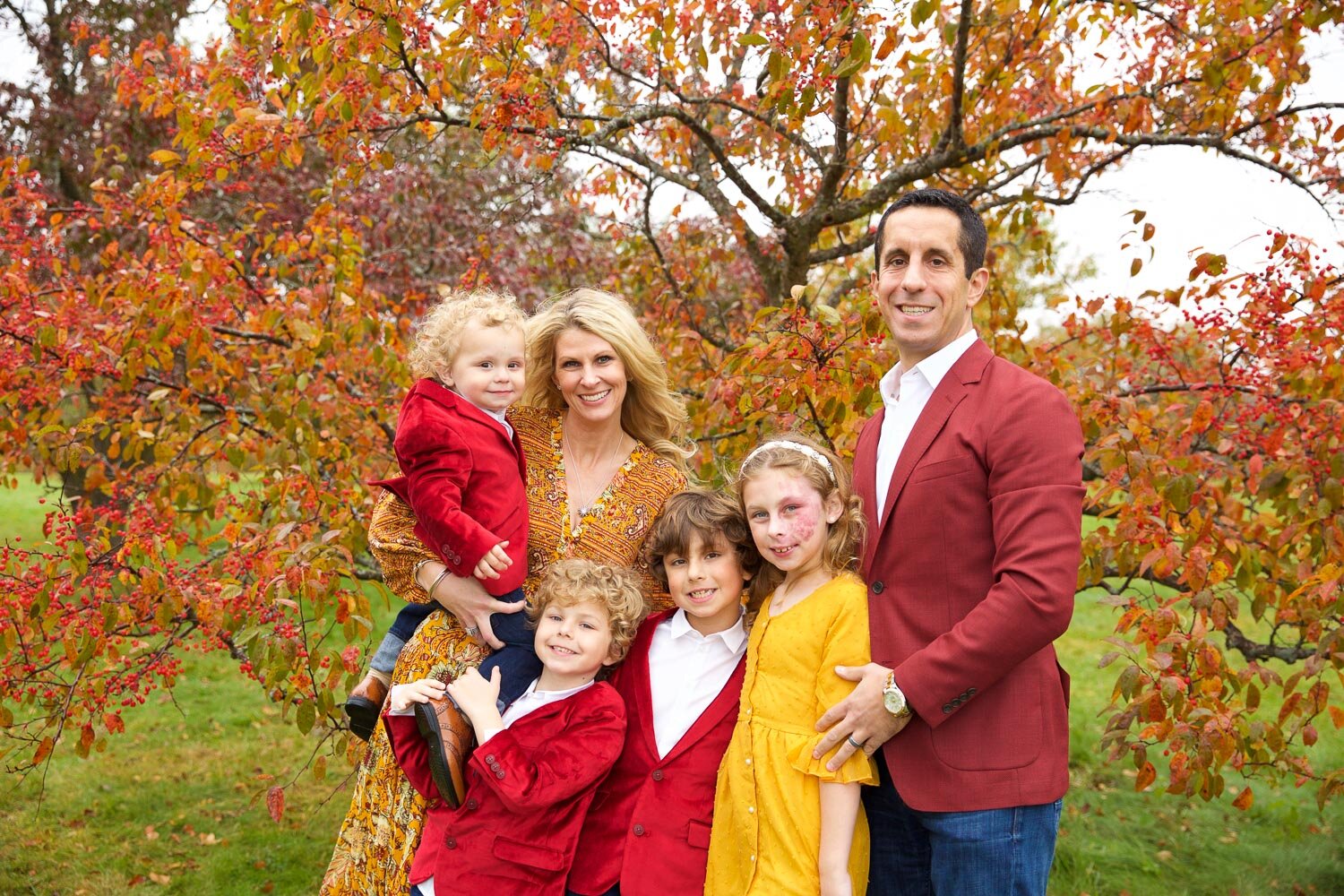 Family of six wearing autumn tones posed in front of vibrant fall foliage in Chanhassen Minnesota