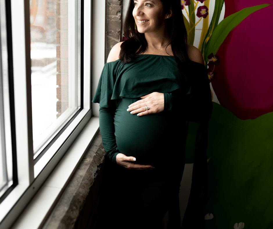 Mother-to-be in an elegant green dress smiling out the window during maternity photos