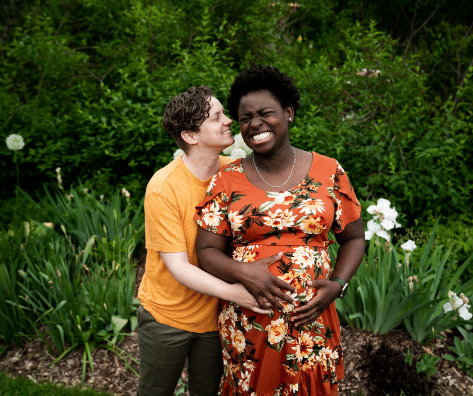 Mom in yellow shirt and Momma in orange flower maternity dress smiling and laughing at the Lyndale rose garden