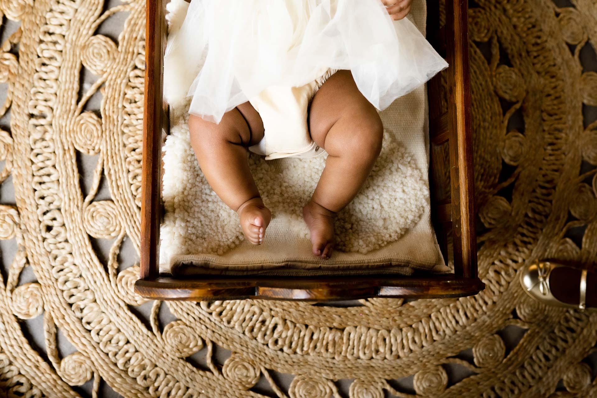a baby's feet against cream canvas fabric, posed in a wooden crib for newborn photography