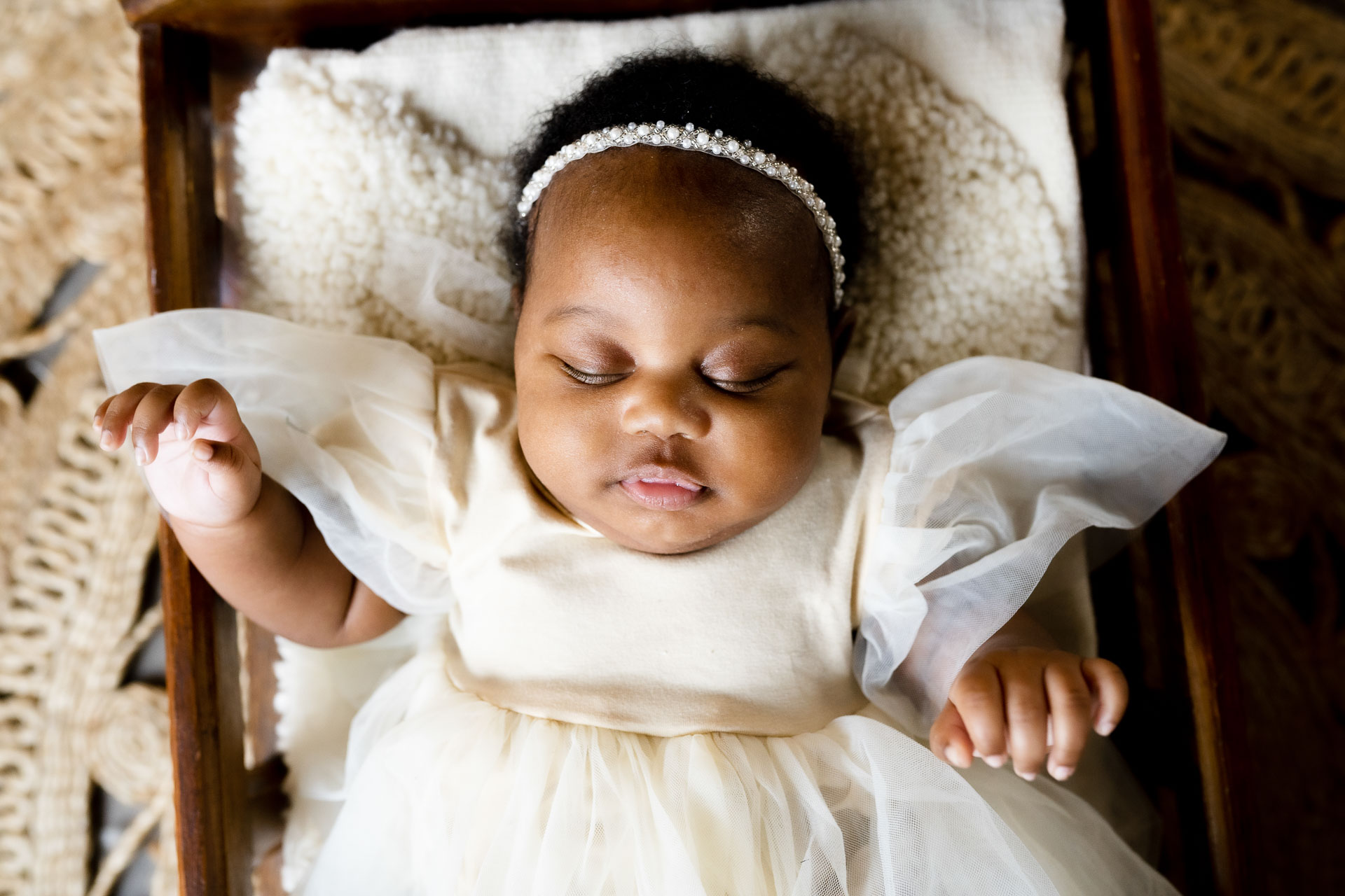 sleeping black baby girl posed in a wooden crib wearing a white dress