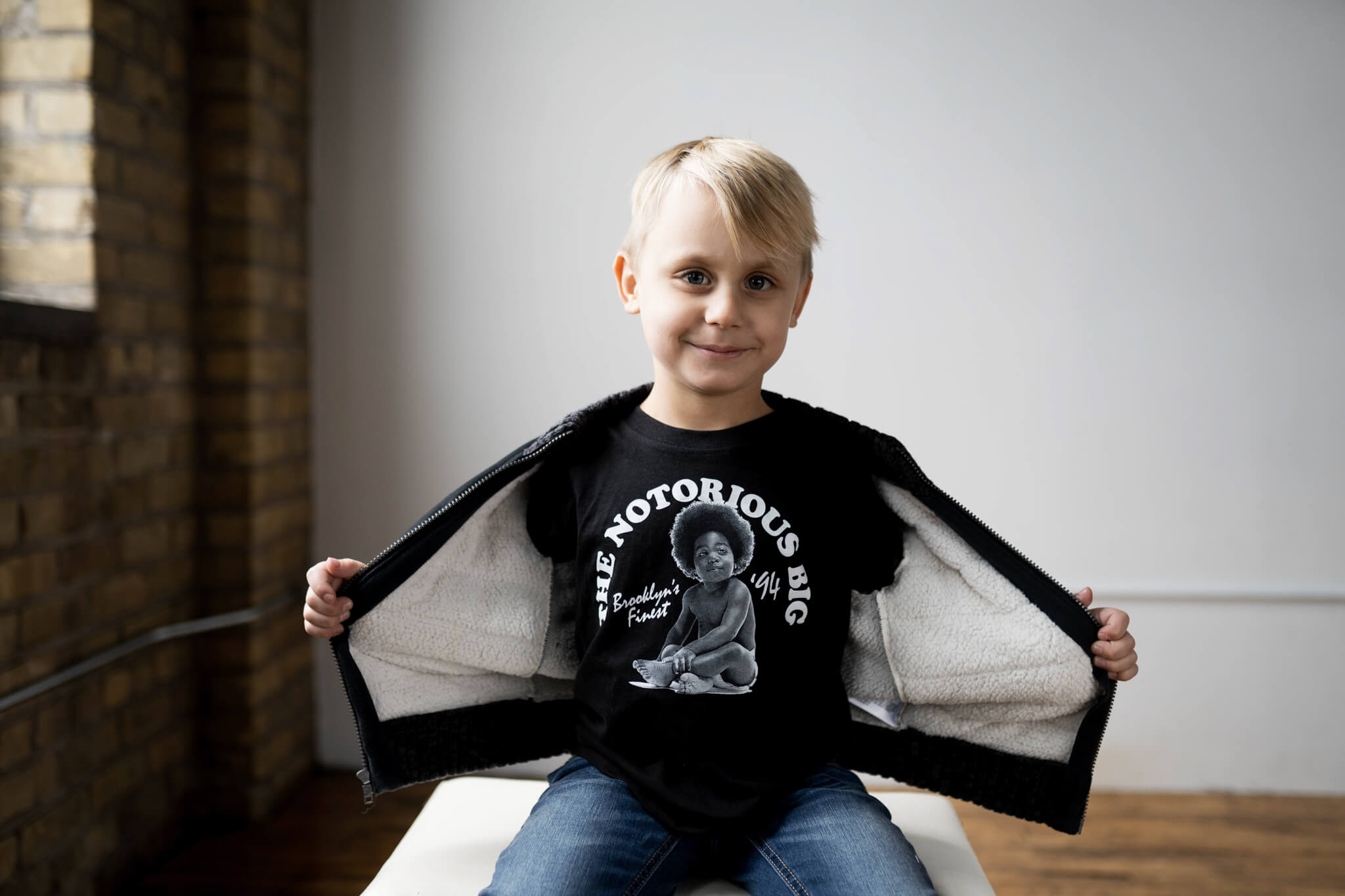 a young boy holding open his jacket to show off his "The Notorious Big" shirt underneath