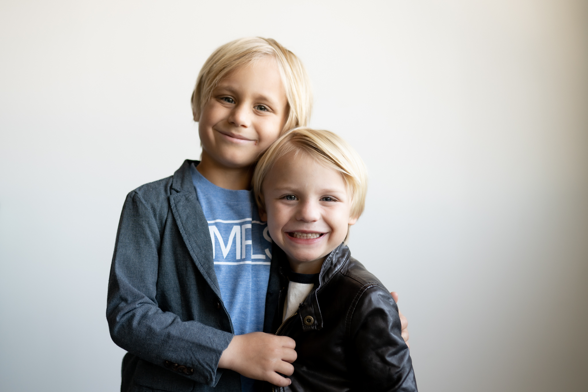 Two blond brothers smiling widely into the camera during a family photoshoot