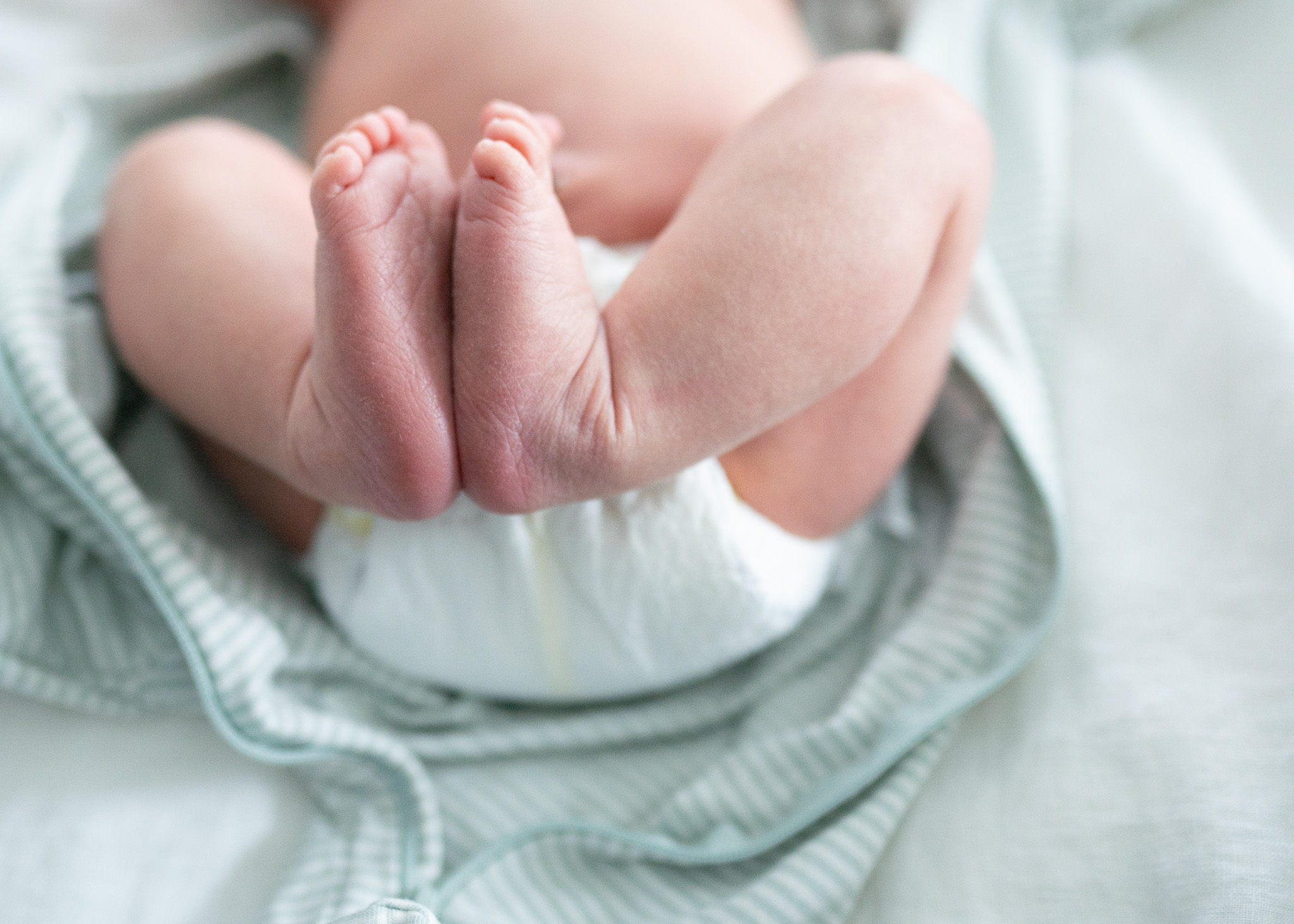 Newborn baby feet on sage blanket wearing a white diaper