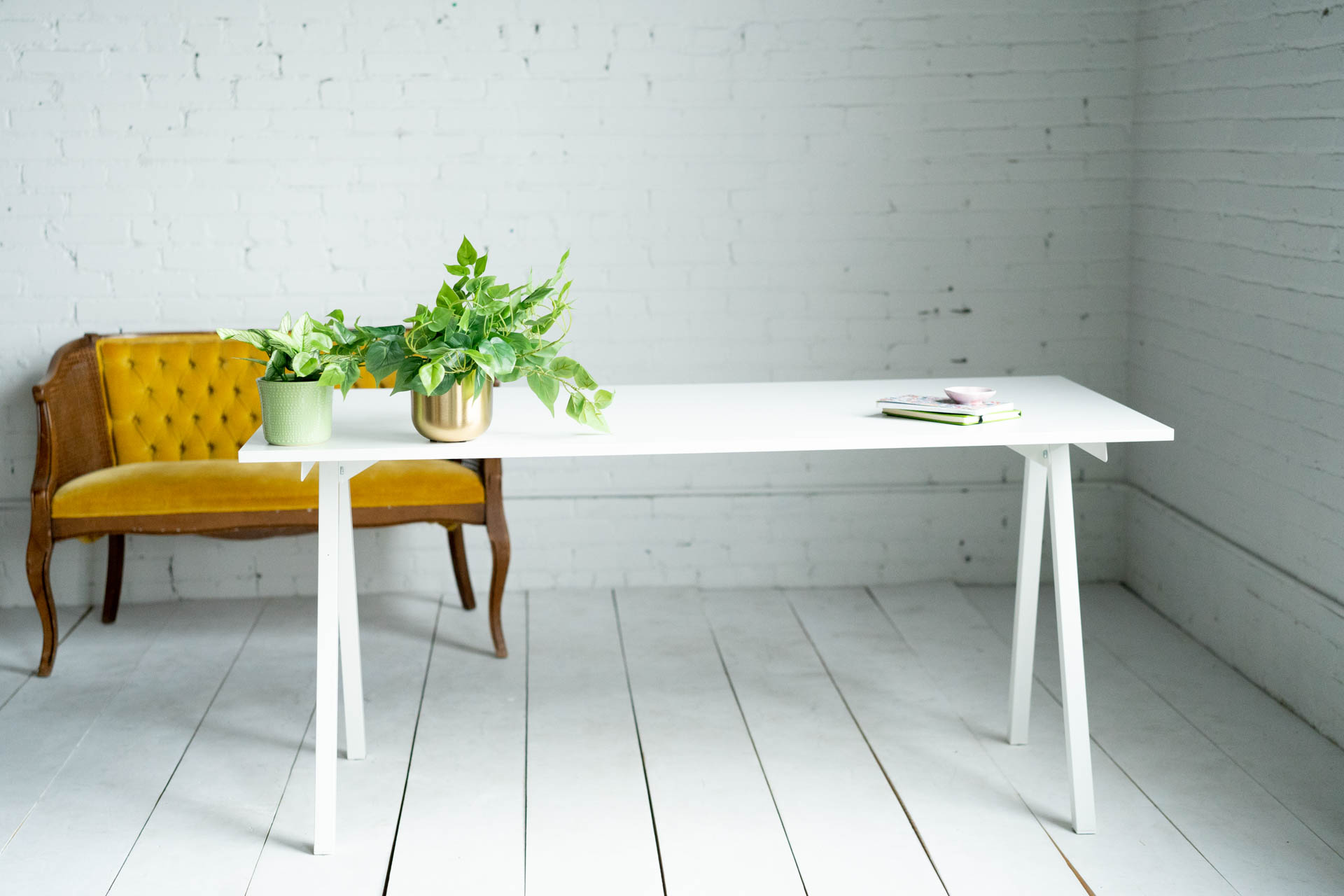 a clean white office desk with plants on the surface, against a white brick wall