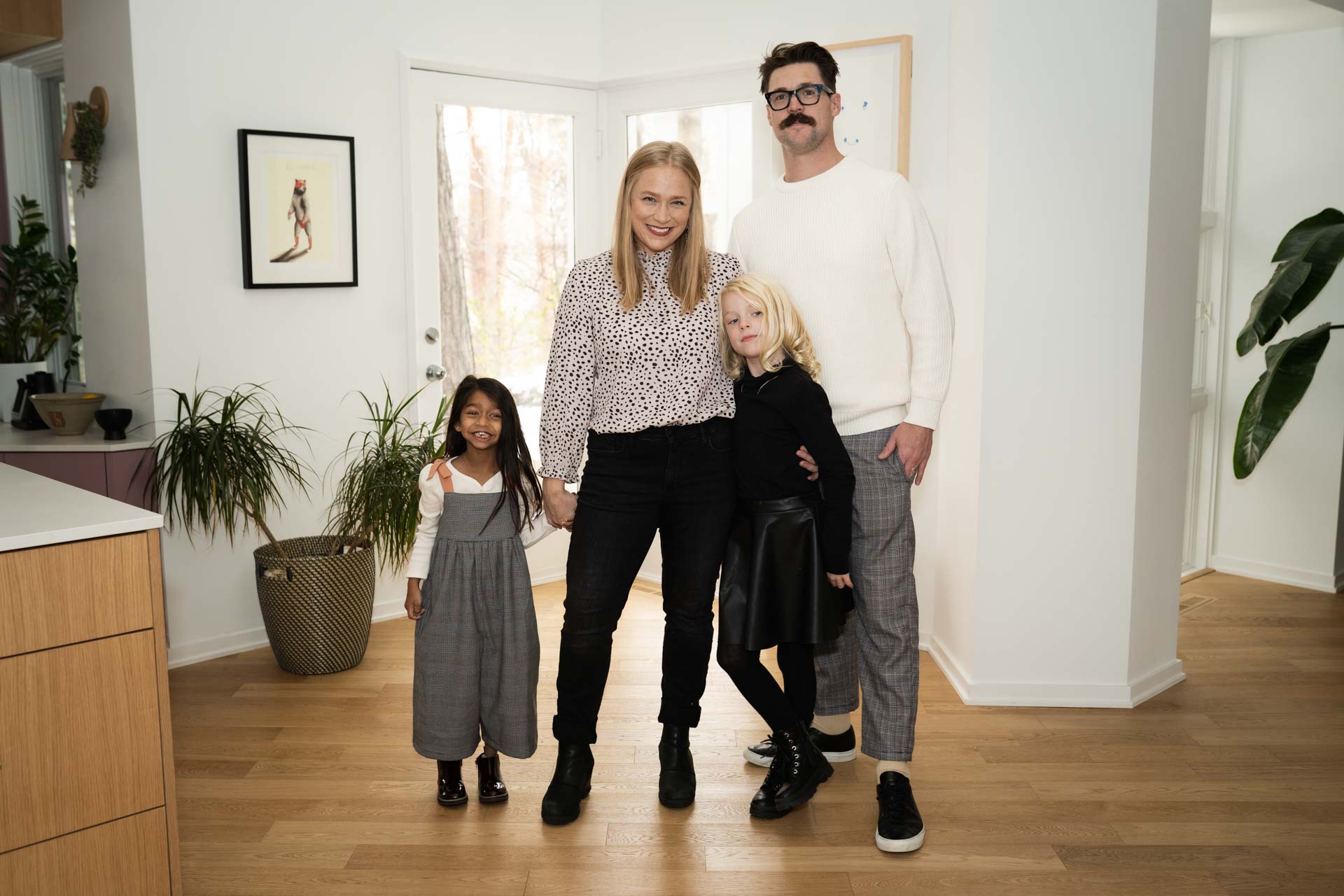 Family of four, standing together in their neutral, stylish Minneapolis home