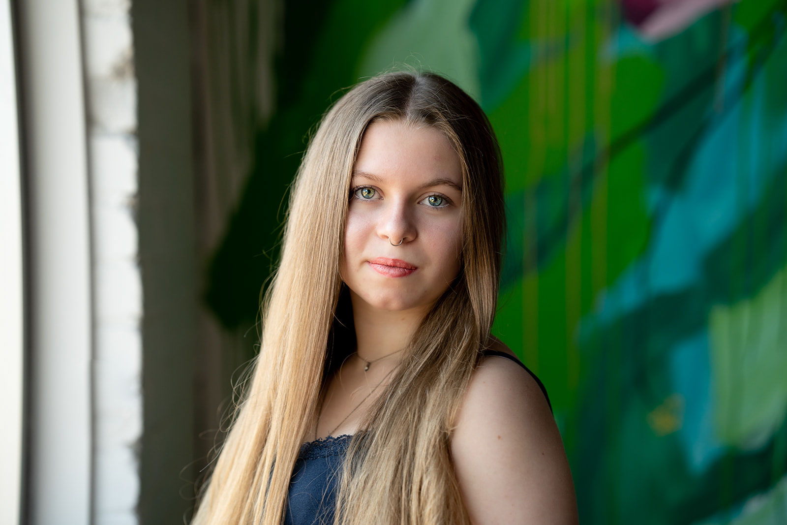 high school senior looking intently into the camera with hazel eyes, in front of a vibrant green and blue mural