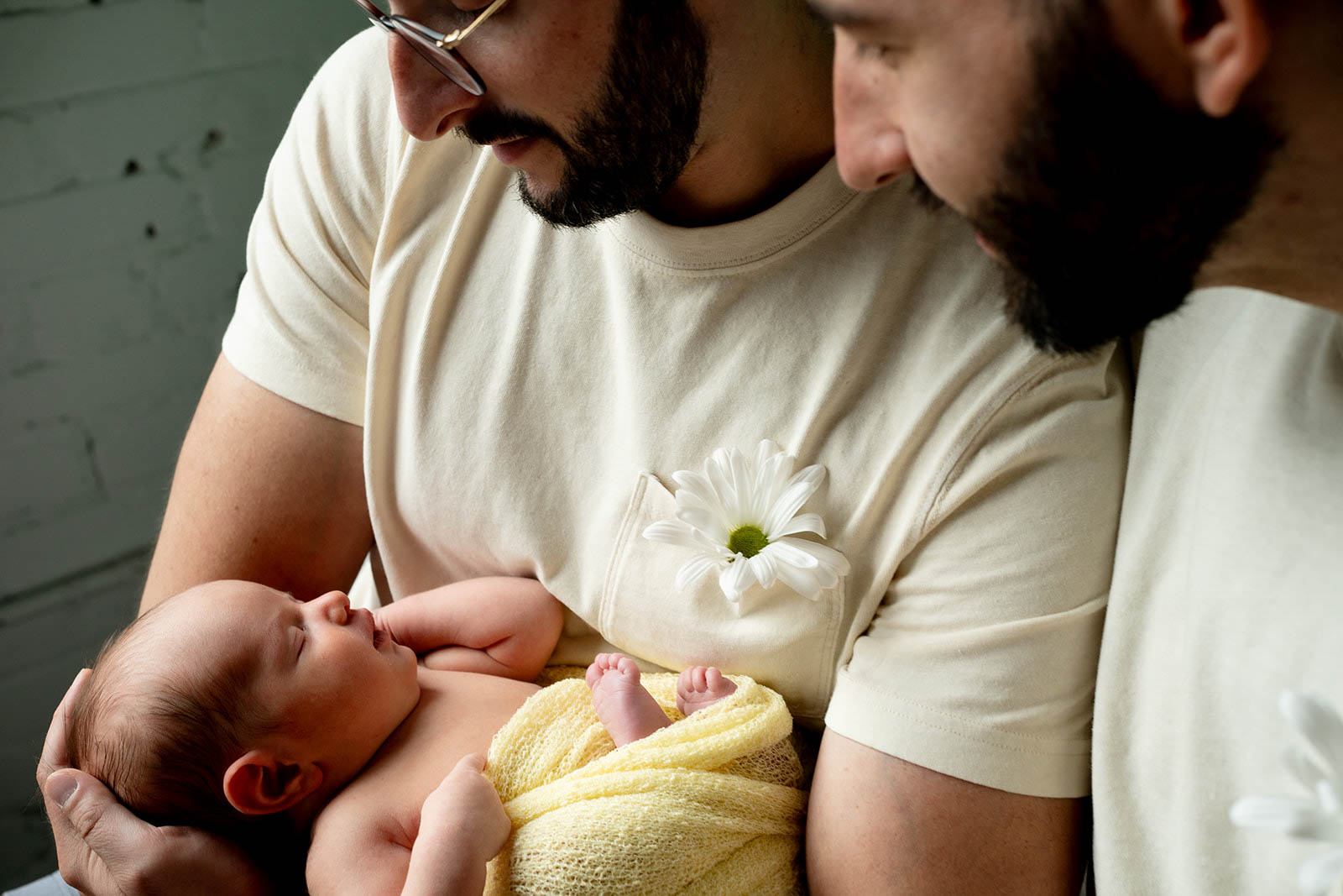 Kenneth Marks's Project Two fathers looking down at their newborn baby, who is wrapped in a yellow blanket and sleeping peacefully in their arms