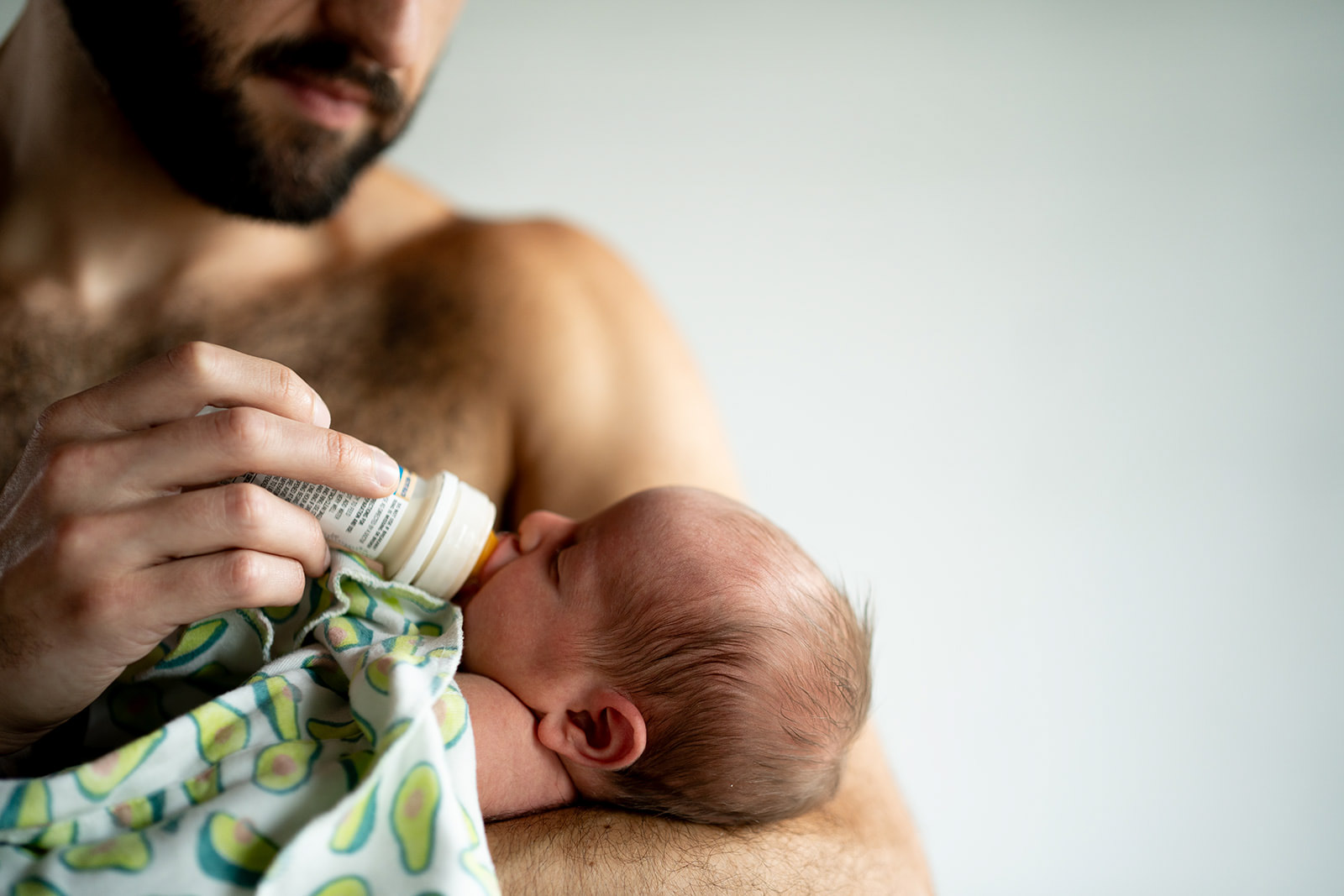 Kenneth Marks’s Project A father bottle feeding their newborn baby in the cradle of their arms at a newborn photo session