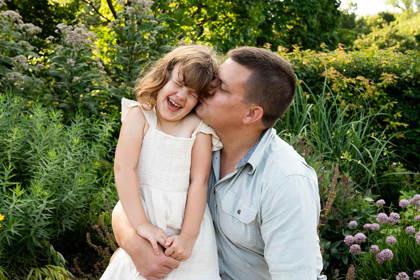 a young girl kisses her younger brother on the cheek while they lean against a rustic wall and smile