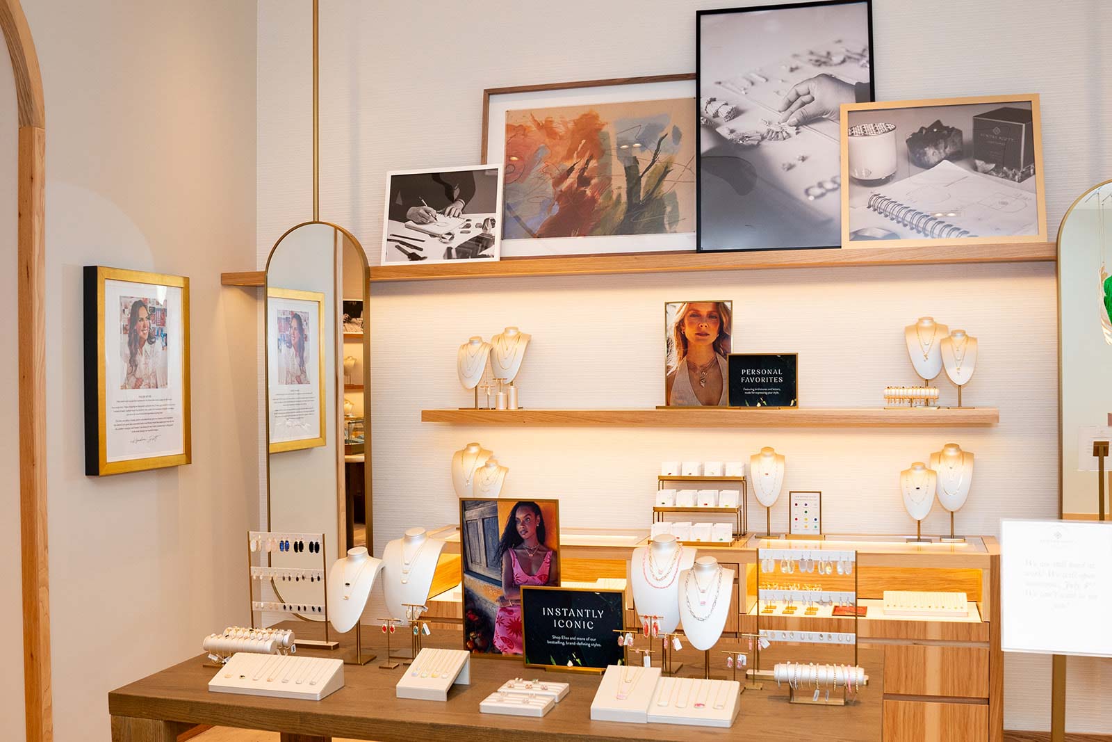 two vibrantly dressed businesswomen smiling and laughing back to back in front of a white brick wall covered in fresh taped flowers