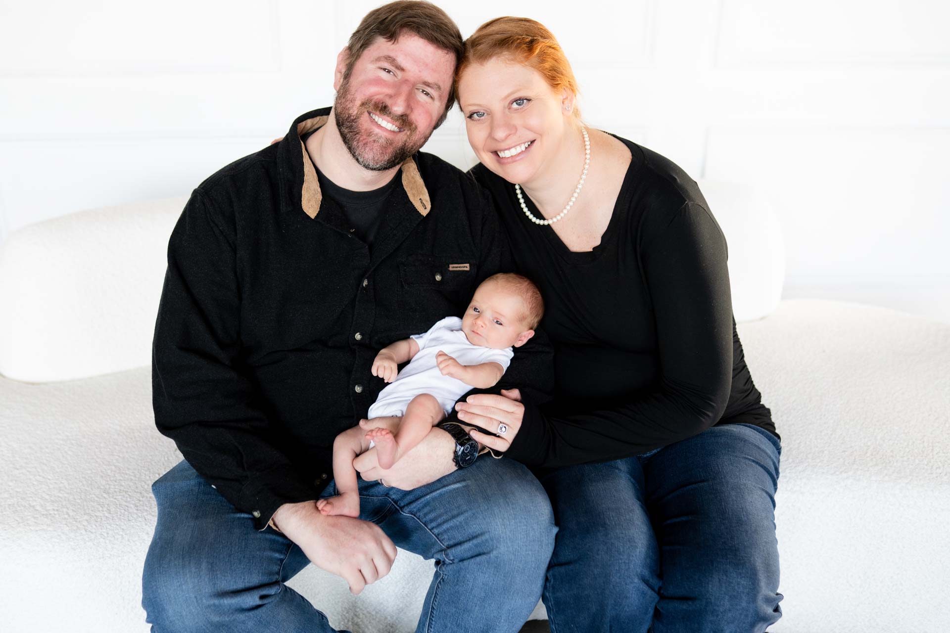 a mother in a white shirt and jeans holding her toddler in the air and kissing her on the cheek, while the sun shines down on them at golden hour in a wildflower garden